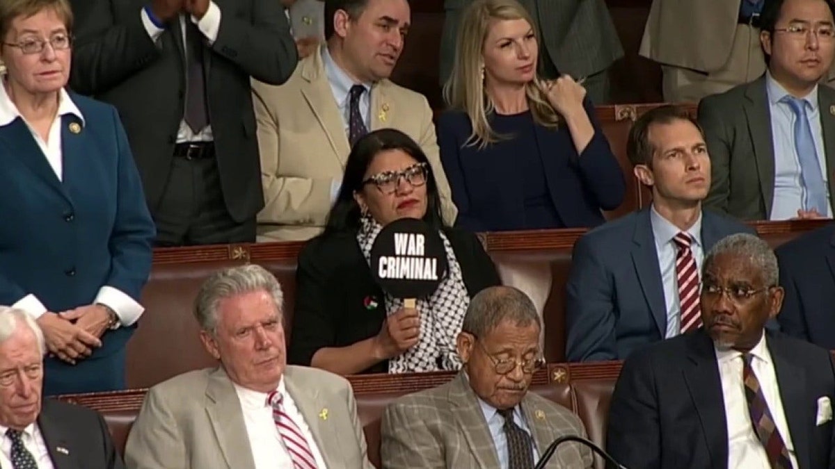 Rashida Tlaib holding up a sign that says war criminal