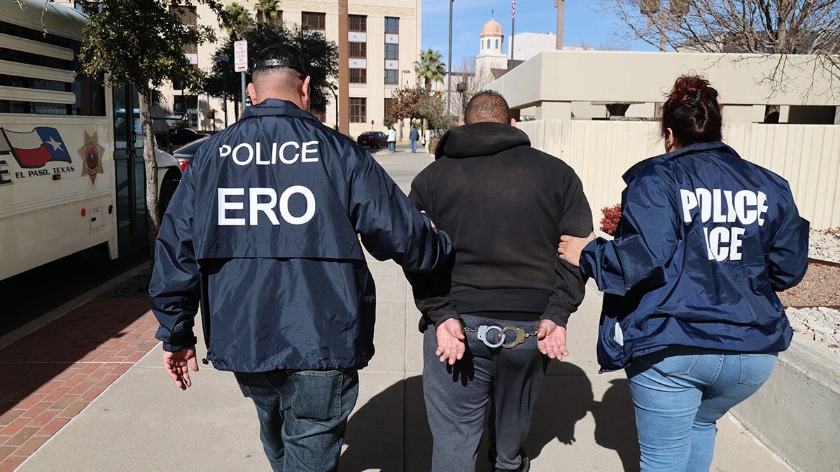 Male ICE officer and female officer walking with cuffed male