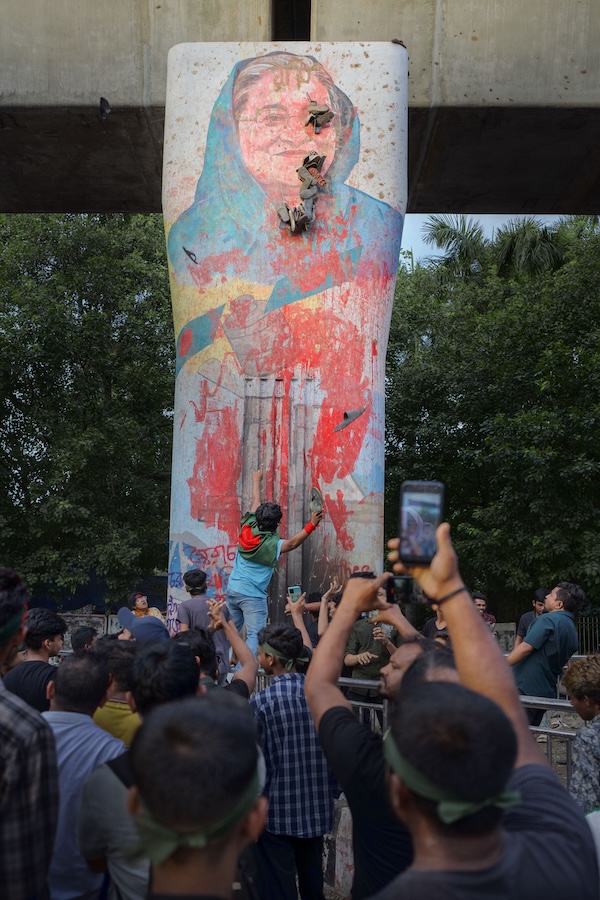 Student protesters throw shoes at a mural of Sheikh Hasina at Dhaka University, expressing their anger over political turmoil and government policies. The protesters are demonstrating their frustration with the government's handling of recent events, including the controversial quota reforms and the violent clashes with police. Credit: Mohammad Rakibul Hasan