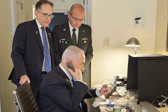 Benjamin Netanyahu speaks on a phone with officials standing behind him 