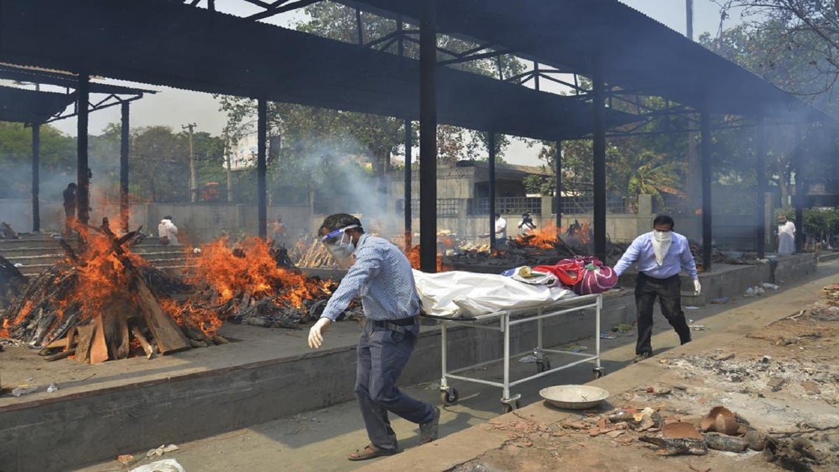 Relatives carry the body of a person who died of COVID-19 as multiple pyres of other victims burn at a crematorium in New Delhi, India, in 2021.