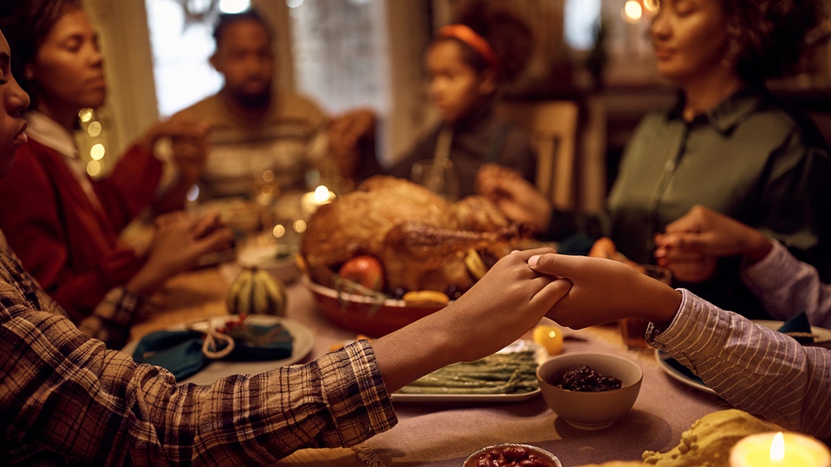 family holds hands at Thanksgiving dinner table