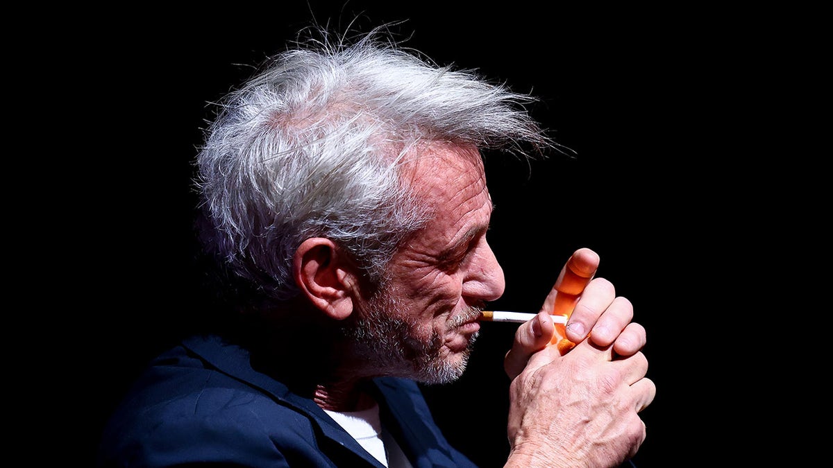 Sean Penn holds a lighter to smoke a cigarette during a press conference at a film festival.