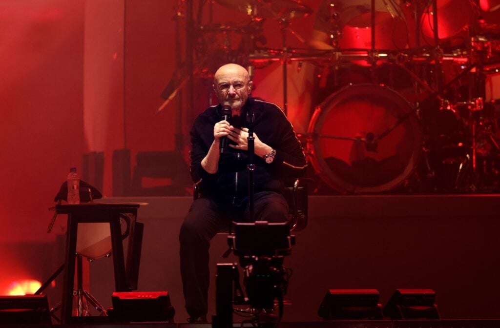 Phil Collins on stage, illuminated in red, in March of 2022.