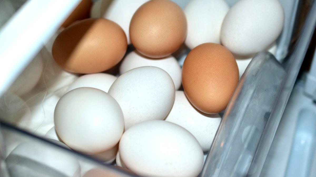 A variety of white and brown eggs are seen in a refrigerator compartment.