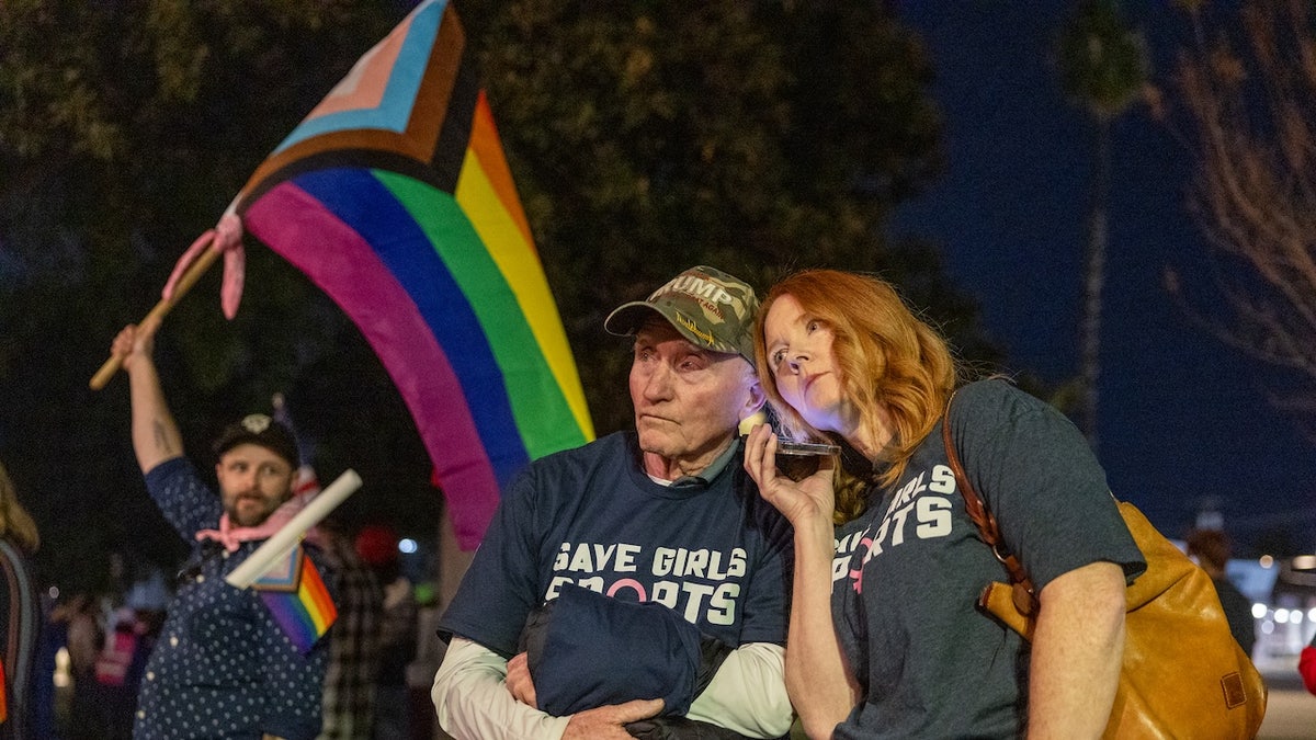 Transgender athlete supporter Kyle Harp, left, of Riverside holds the progress pride flag as 'Save Girls Sports' supporters Lori Lopez and her dad Pete Pickering, both of Riverside, listen to the debate as they join the overflow crowd converging outside the Riverside Unified School District meeting Thursday night to debate the rights of transgender athletes to compete in high school sports, Thursday, Dec. 19, 2024.