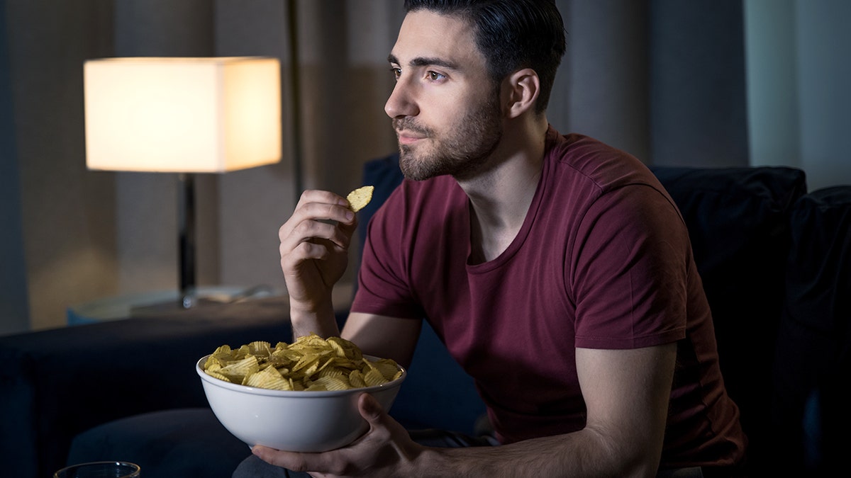 Young man relaxing by watching movie eating chips.