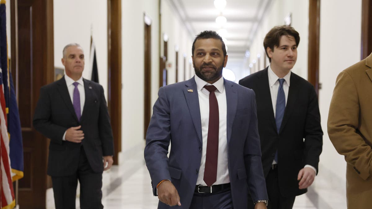 Kash Patel walking down a hallway wearing a suit