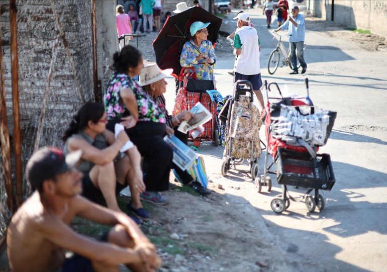 People sit in the shade next to a wall in Villa Fiorito