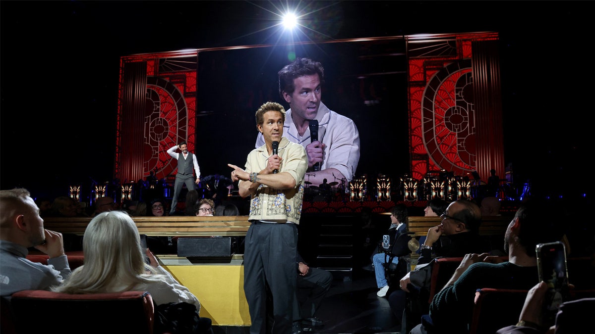 Ryan Reynolds holds the microphone for a tribute to Hugh Jackman mid-show