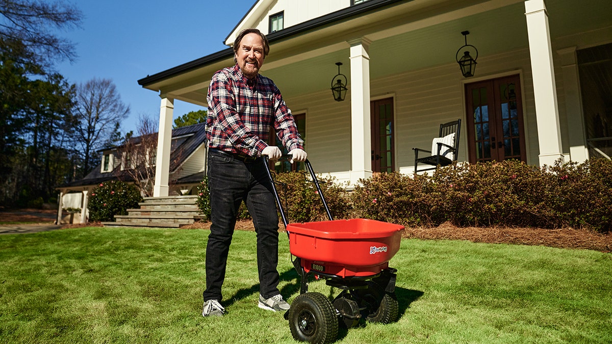 Richard Karn with a fertilizer spread walking on a lawn